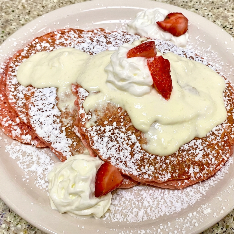 Stack of pancakes topped with vanilla cream, whipped cream, strawberries, and powdered sugar on a plate.